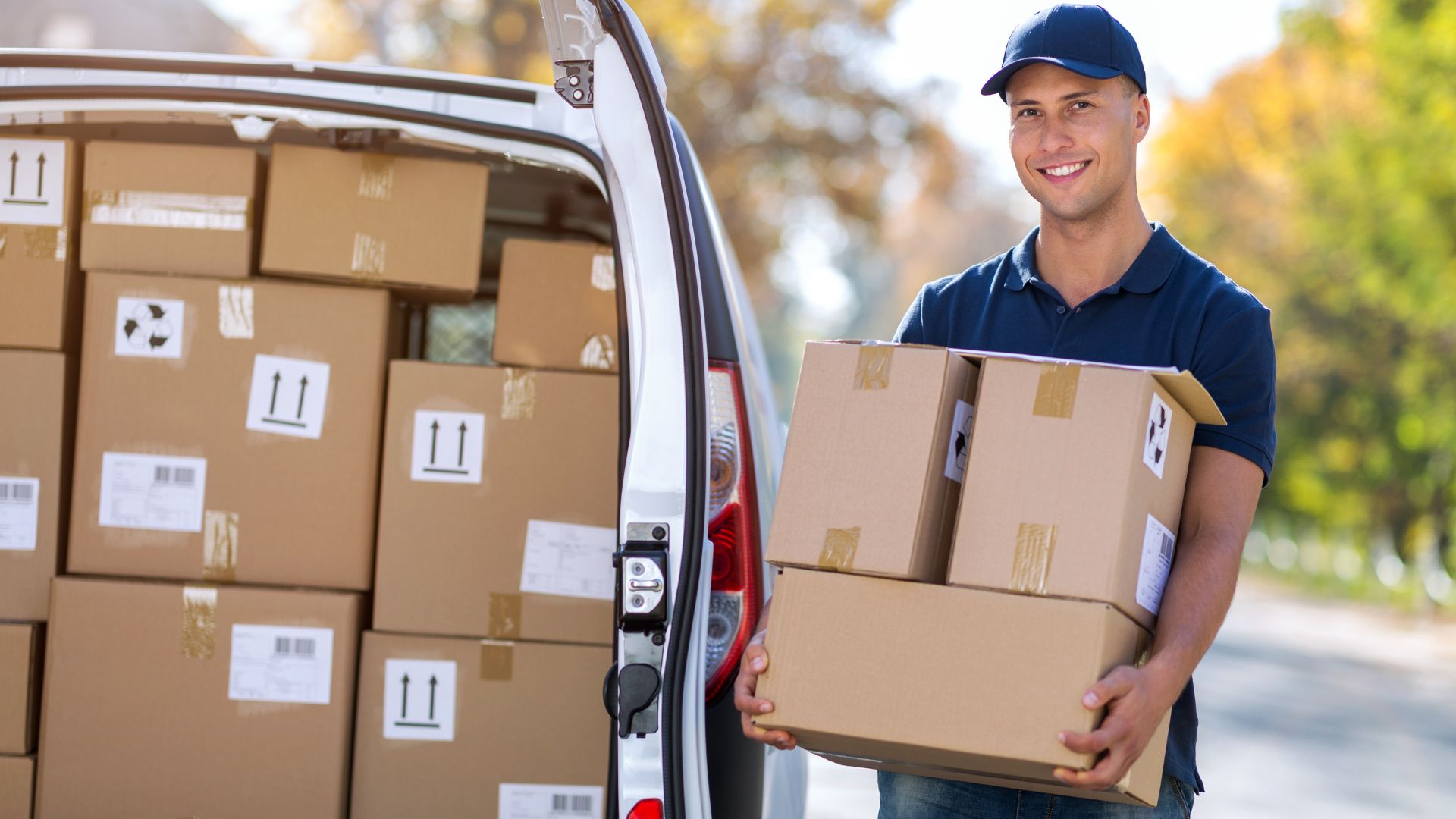 Smiling delivery person holding packages next to van full of boxes