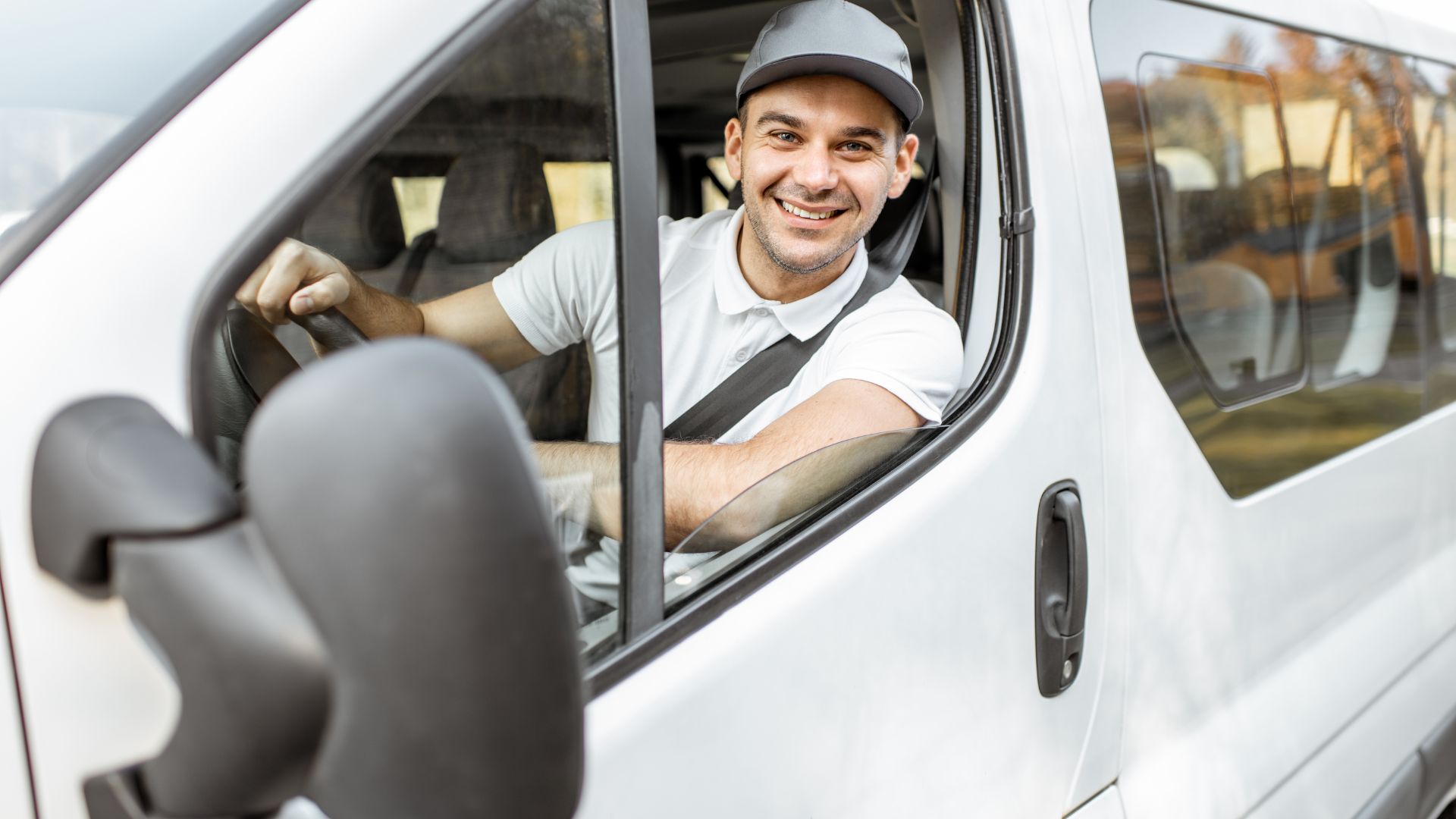 Smiling delivery driver sitting in white van wearing cap and white shirt