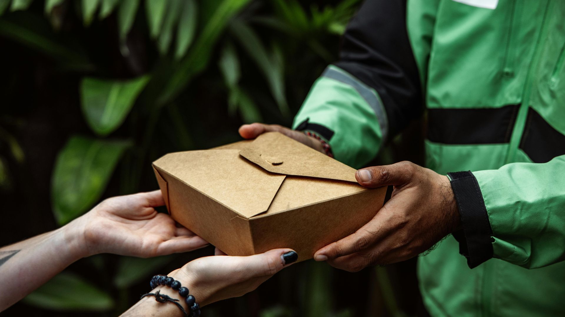 Hands exchanging a brown paper delivery box against green leafy background