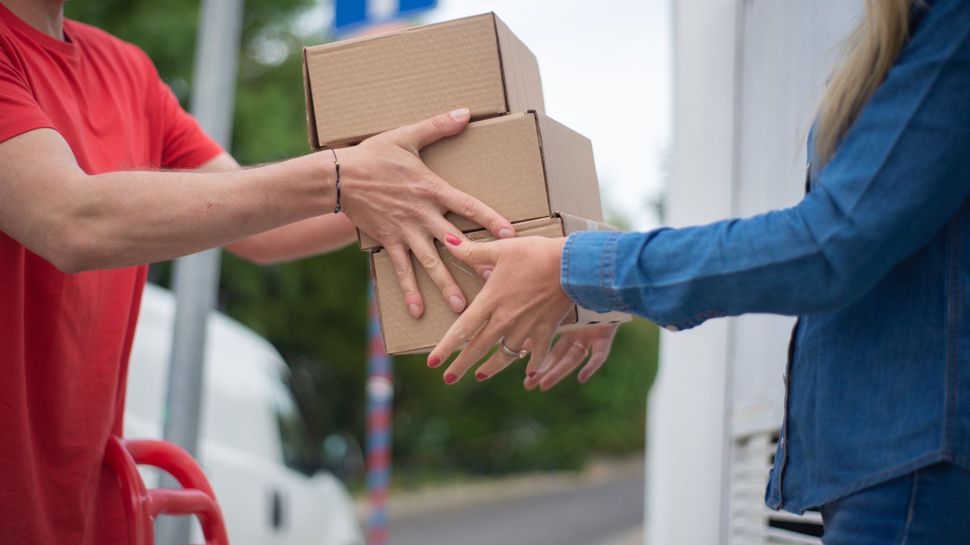 Delivery person handing cardboard packages to another person outside