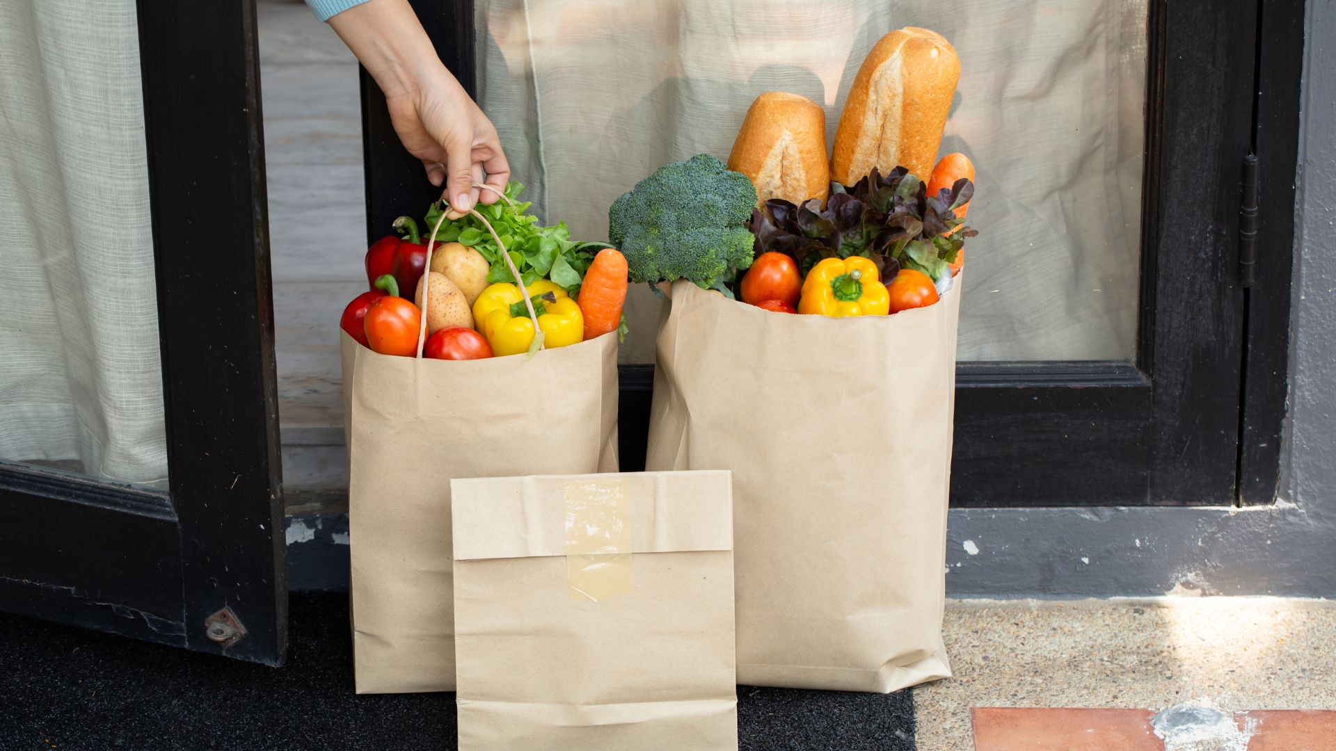 Two paper bags filled with fresh vegetables, bread, and produce