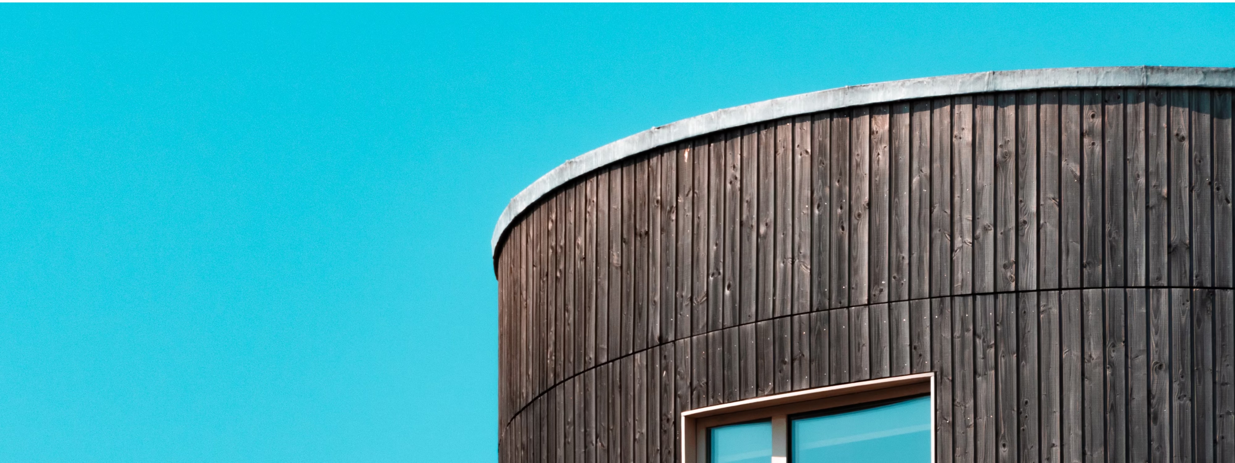 Curved wooden building with window against bright turquoise blue sky